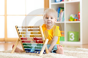 Preschooler baby learns to count. Cute child playing with abacus toy. Little boy having fun indoors at kindergarten