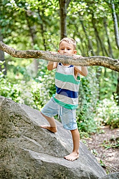 Preschooler boy climbs on rock against blurry green trees