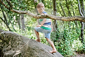 Preschooler boy climbs on rock against blurry green trees