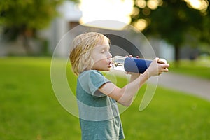 Preschooler boy drinking bottle of water on hot sunny summer day in the backyard or public park. Feeling of thirst. Healthy