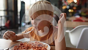 Preschooler boy eating pasta with tomatoes in cafe or restaurant. Healthy/unhealthy food for little kids