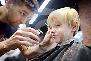 Preschooler boy getting haircut in barbershop. Children hairdresser with professional tools - comb and scissors. Cutting hair for