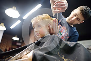 Preschooler boy getting haircut in barbershop. Children hairdresser with professional tools - comb and scissors. Cutting hair for