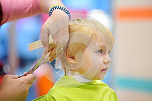 Preschooler boy getting haircut. Children hairdresser with professional tools - comb and scissors.