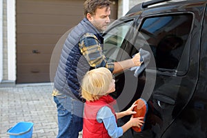 Preschooler boy helping his father washing family car. Little dad helper. Family with children spends time together