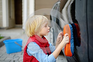 Preschooler boy helping his father washing family car. Little dad helper. Family with children spends time together