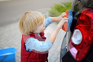 Preschooler boy helping his father washing family car. Little dad helper. Family with children spends time together