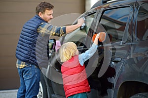Preschooler boy helping his father washing family car. Little dad helper. Family with children spends time together