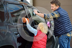 Preschooler boy helping his father washing family car. Little dad helper. Family with children spends time together