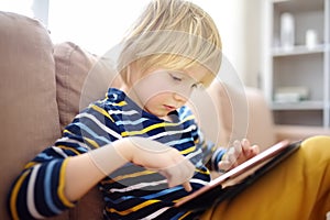 Preschooler boy is learning on distance by tablet or playing pc game sitting on couch. Homeschool education and entertainments for