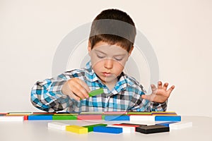 A preschooler boy plays with multi-colored wooden blocks for construction or counting sitting at a table on a white