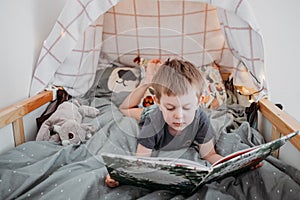 Preschooler boy reading book laying in his bed. spending time at home. Lifestyle family concept