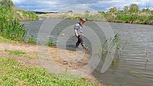 Preschooler boy walks along river bank on spring sunny day. Natural landscape, child in rubber boots walks in water