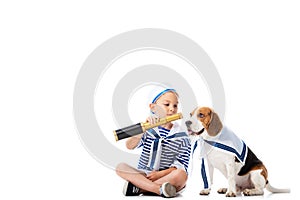 Child in sailor suit holding spyglass while playing with beagle dog isolated on white