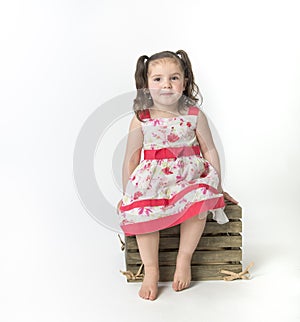 Preschooler in flowered dress siting on wooden box