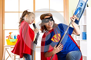 Preschooler girl and her mother dressed like superheroes. Middle-aged woman and kid playing while doing cleanup at home