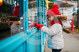 Preschooler girl looking at window glass of large department store decorated for Christmas