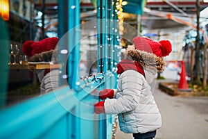 Preschooler girl looking at window glass of large department store decorated for Christmas