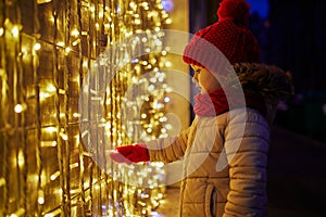 Preschooler girl looking at window glass of large department store decorated for Christmas