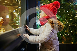 Preschooler girl looking at window glass of large department store decorated for Christmas