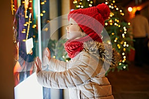 Preschooler girl looking at window glass of large department store decorated for Christmas
