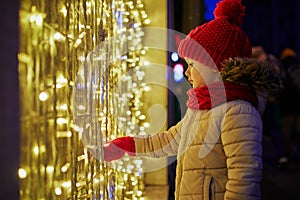 Preschooler girl looking at window glass of large department store decorated for Christmas