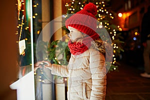 Preschooler girl looking at window glass of large department store decorated for Christmas