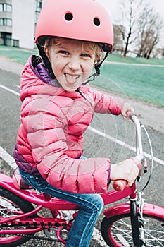 Preschooler girl riding pink bike bicycle in helmet on backyard road outside on spring autumn day