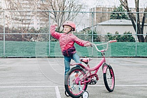 Preschooler girl riding pink bike bicycle in helmet on backyard road outside on spring autumn day