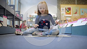 preschooler girl sitting on the floor in municipal library and reading a book