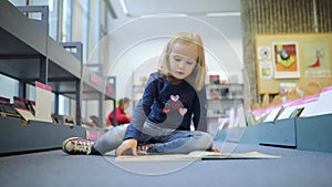 preschooler girl sitting on the floor in municipal library and reading a book