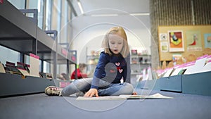 preschooler girl sitting on the floor in municipal library and reading a book