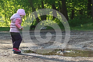 Preschooler girl throwing pebbles into dirt summer