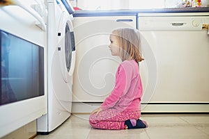 Preschooler girl watching into the washing machine