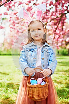 Preschooler girl wearing bunny ears playing egg hunt on Easter