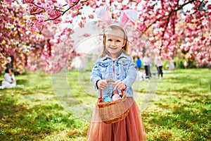 Preschooler girl wearing bunny ears playing egg hunt on Easter