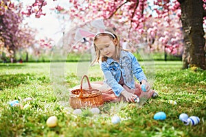 Preschooler girl wearing bunny ears playing egg hunt on Easter