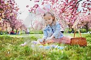 Preschooler girl wearing bunny ears playing egg hunt on Easter