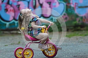 Preschooler girl wearing checked tunic riding yellow and pink tricycle