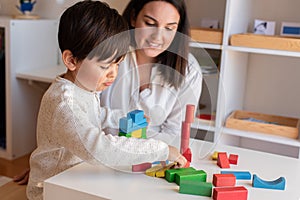 Preschooler Kid playing with wood blocks and teacher educador help. Homeshooling. Learning Community. Montessori School