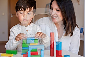 Preschooler Kid playing with wood blocks and teacher educador help. Homeshooling. Learning Community. Montessori School