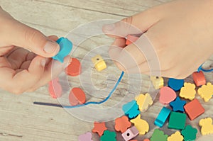 Preschooler making bracelet from thread and wooden colored beads. Development of kids motor skills, coordination and logical