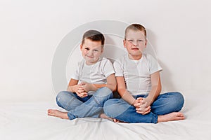 Preschoolers in jeans and T-shirts sit on the bed of the house and look into the camera