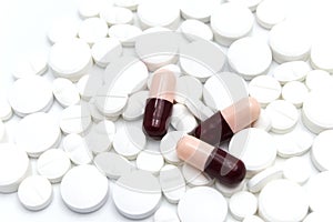 Prescription drugs, pills and tablets of different colors between red and dark gray colors all mixed in a capsules and white table