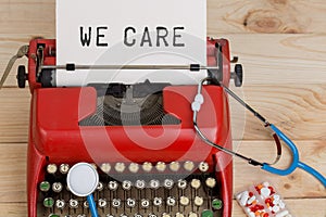 Prescription medicine or medical diagnosis - doctor workplace with blue stethoscope, pills, red typewriter with text We care