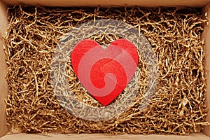Present box with big red heart lying on brown shredded craft paper filler