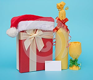 Present box covered by santa claus hat and wrapped wine with blank card for text