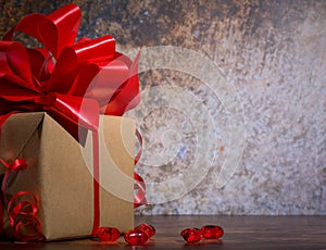 Present box with red bow ribbon and shinny little hearts on a wooden rustic board for Valentines day