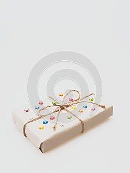 A present or gift box wrapped by rough brown recycled paper and tied with brown hemp rope as ribbon with multi color star isolated