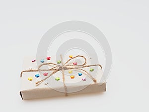 A present or gift box wrapped by rough brown recycled paper and tied with brown hemp rope as ribbon with multi color star isolated